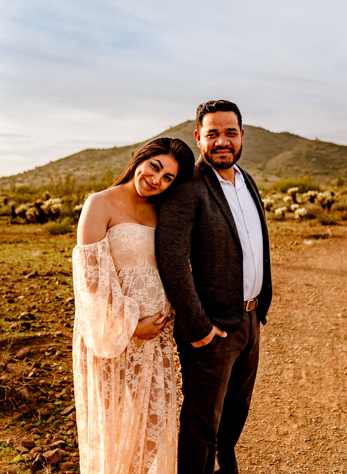 mom wearing pink lace, boho dress while hugging husband, smiling taken by Arizona photographer, Amber Herrera