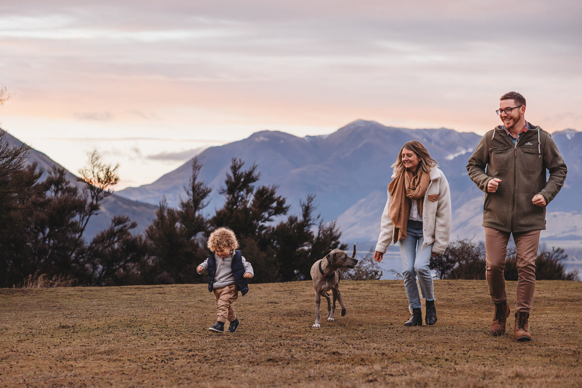 family running around in the grass with mountains in the background captured by Bie during a wanaka family photography session