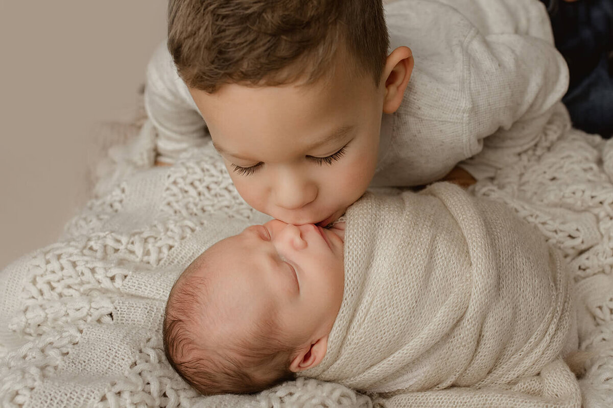 brother leaning over baby and kissing his cheek