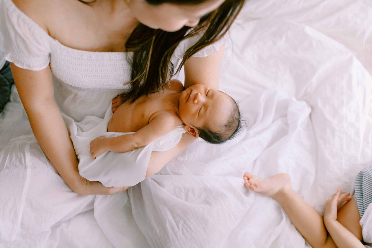 newborn son being held by his mom while his sister's foot sticks into the photo