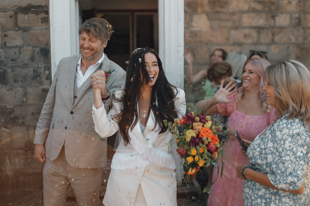 A wedding photographer captures the magical moment of a bride and groom exiting a building, surrounded by joyful confetti.