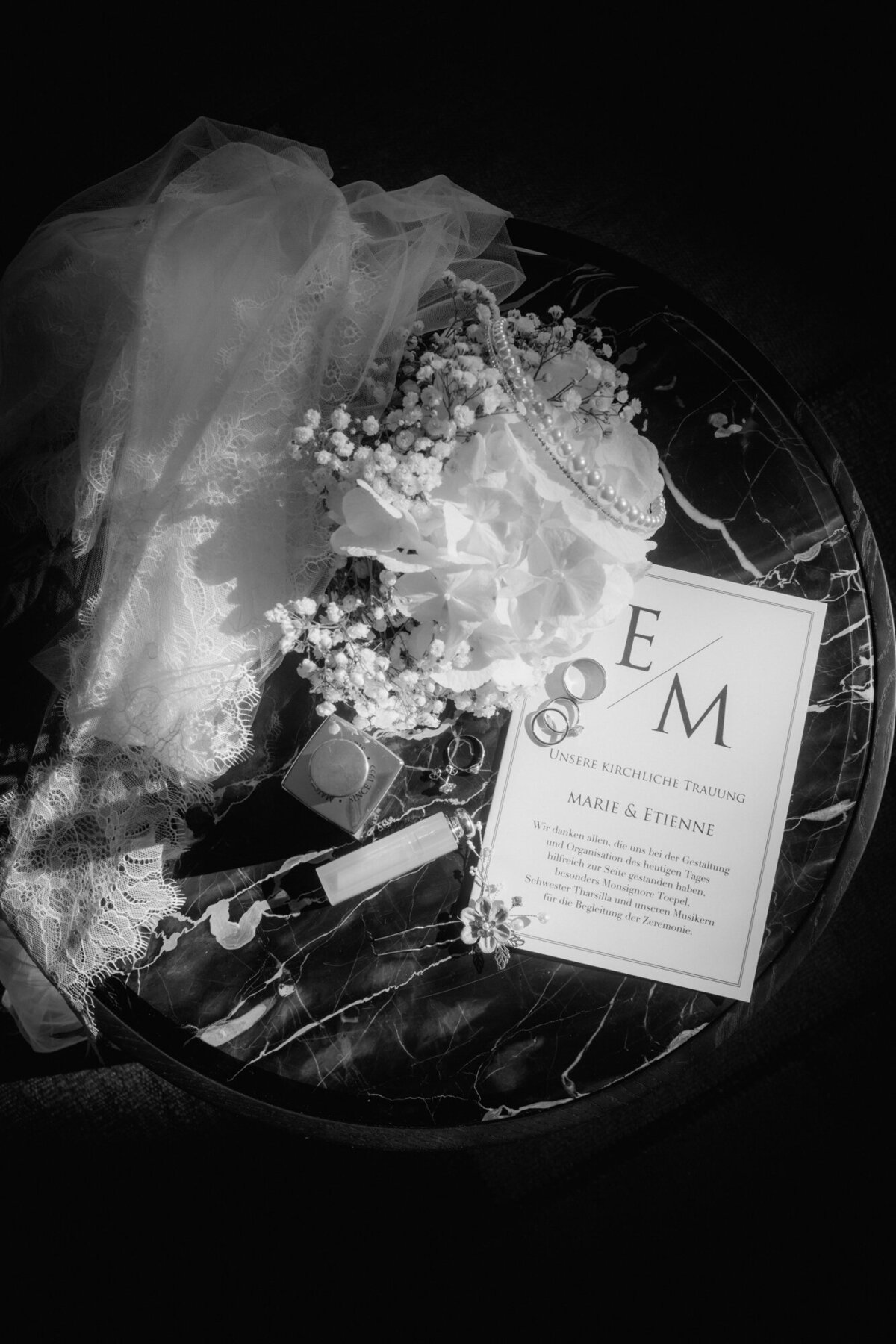 Flowes, wedding veil, stationery and rings are artistically arranged on a small round table.