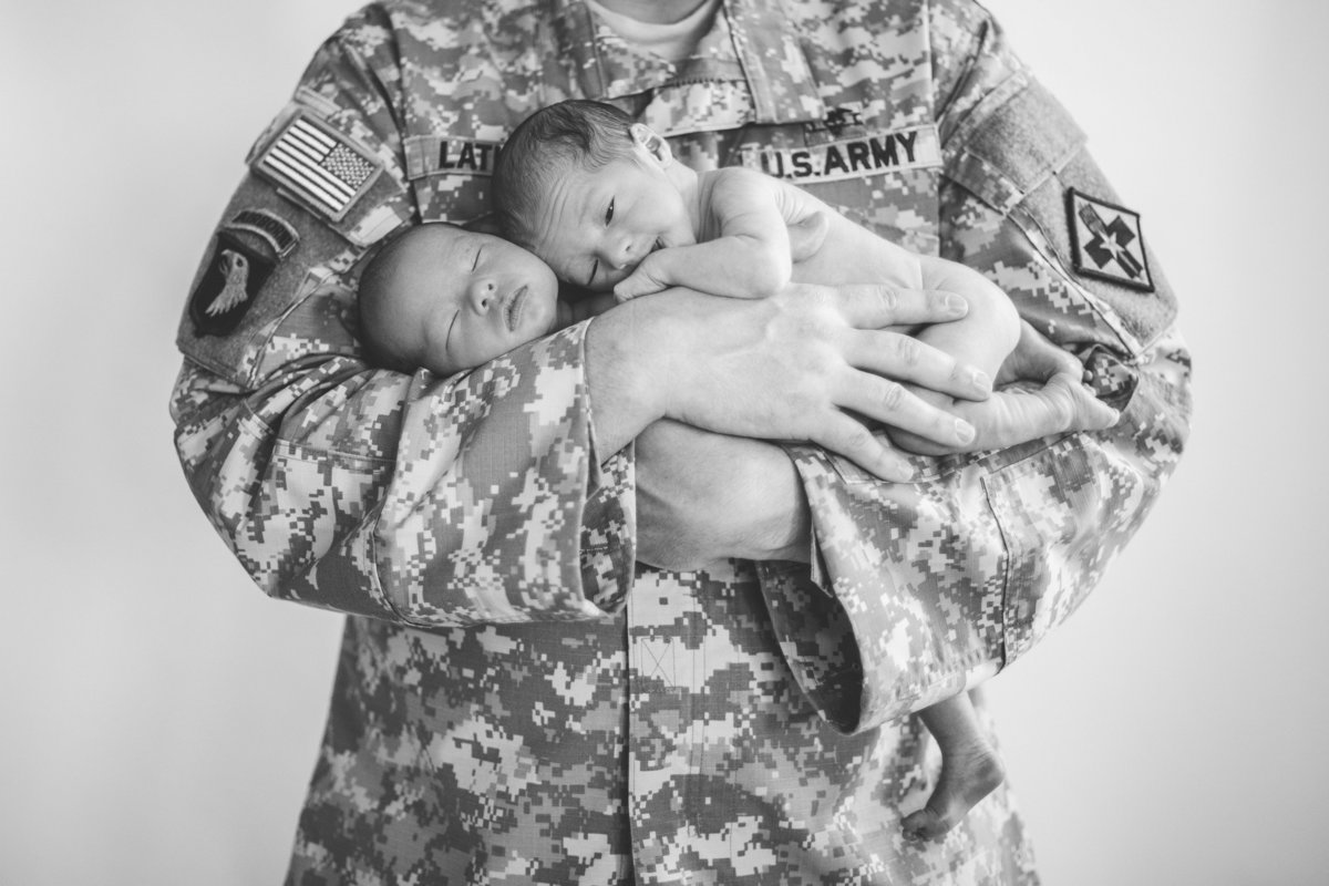 Newborn photography session of twins being held by their father who is a soldier in the military.