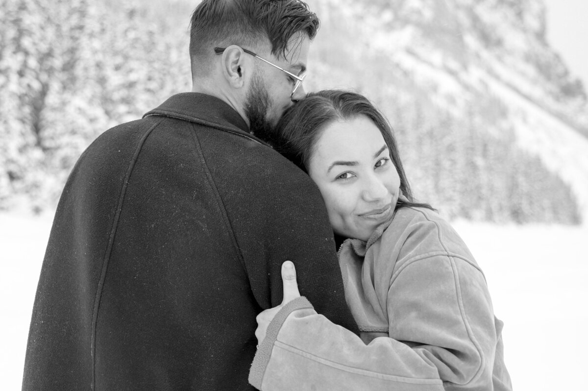 Couple embraces and smiles with snowy backdrop in Banff.