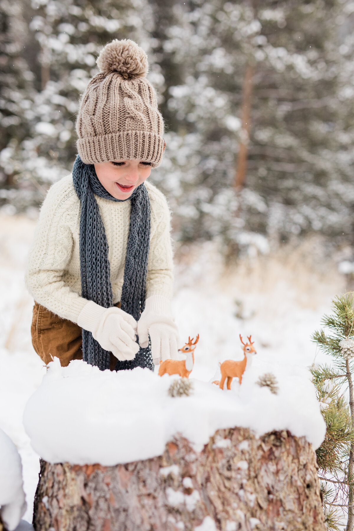 A young boy has his toy reindeer in front of him. He is playing with them in a snow covered field.