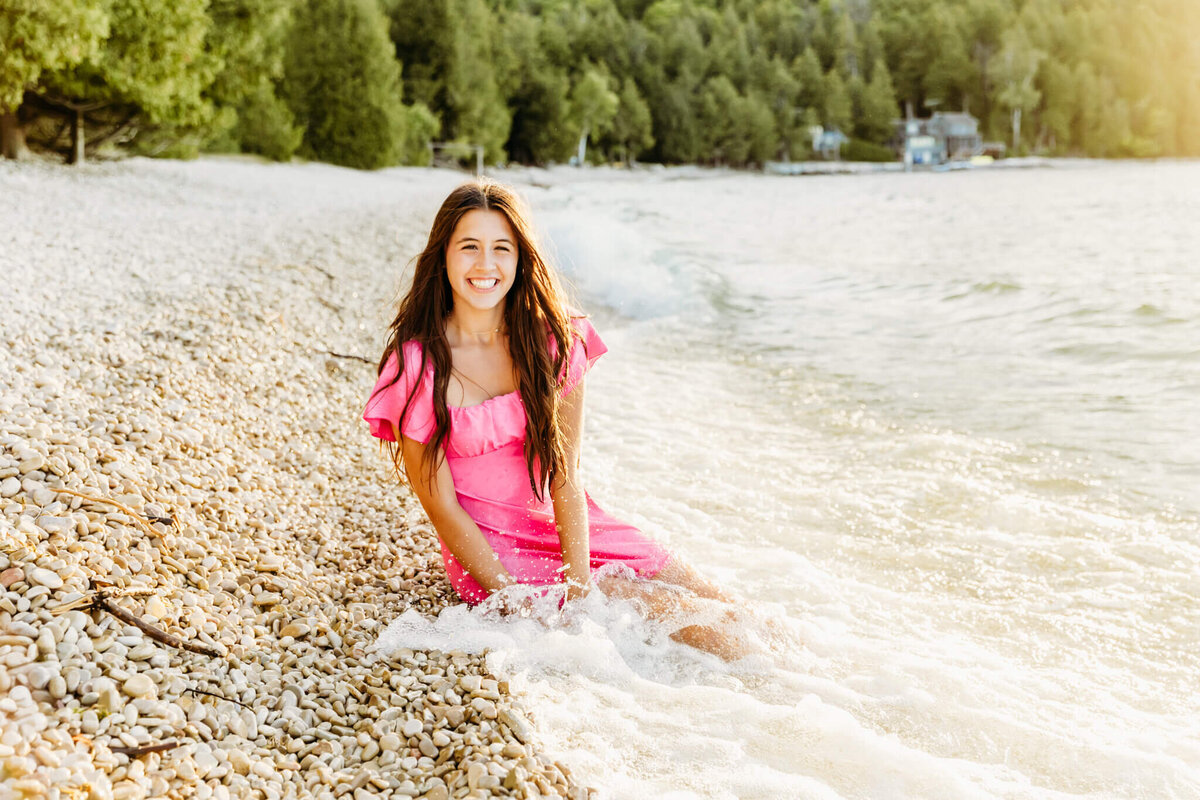 pretty high school girl laughing as she sits on a rocky beach and the waves crash over her in Door County