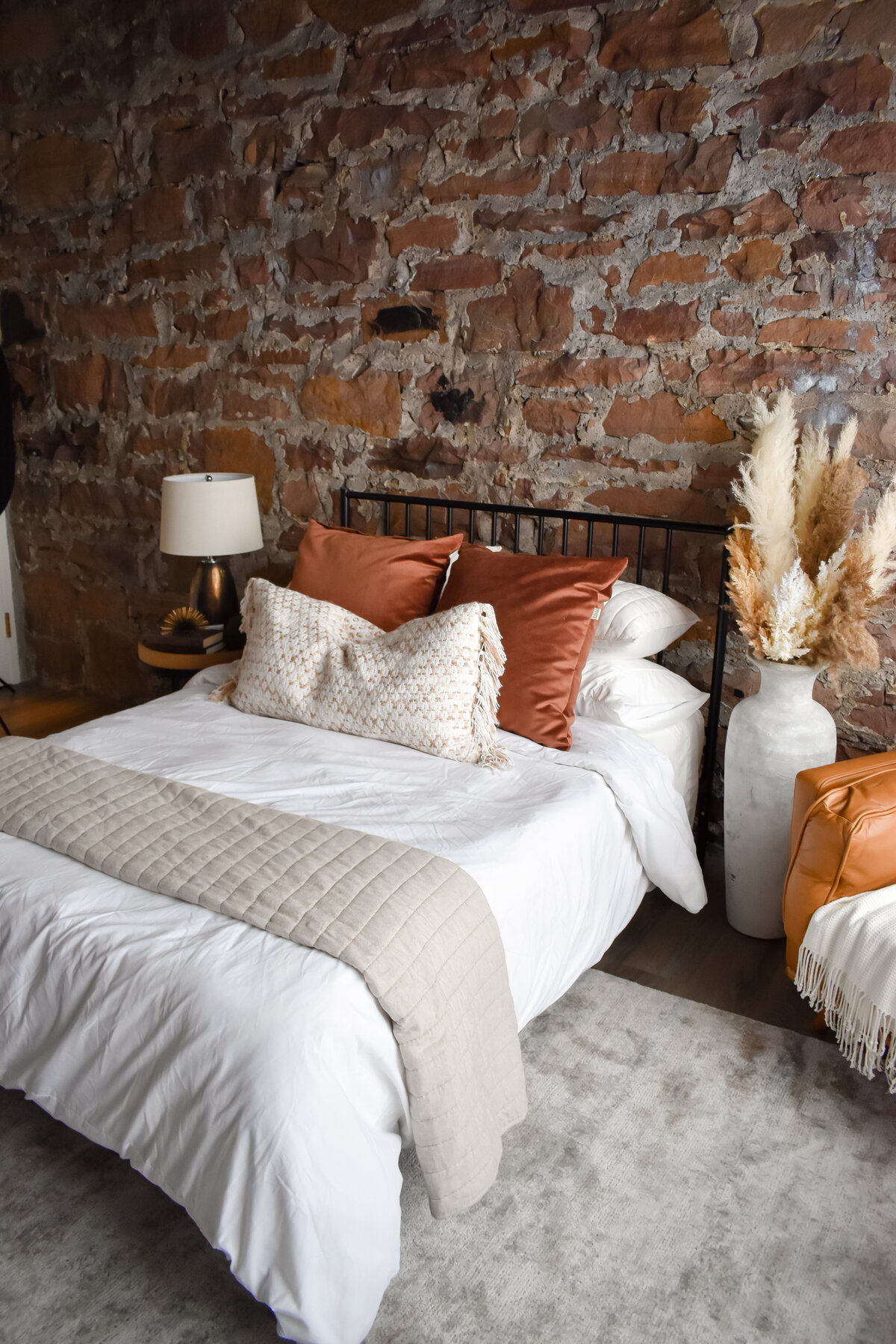 A bed with a white duvet and white and burnt orange throw pillows