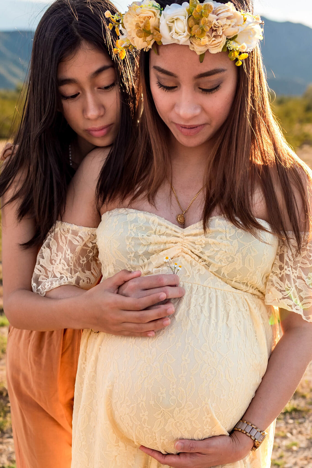 Teen daughter hugging pregnant mom while they look down on baby-to-be. Photo by Cactus & Pine Photography
