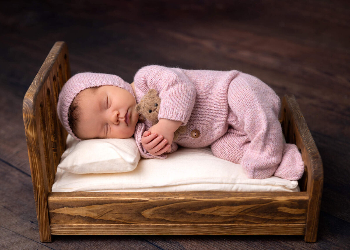 newborn baby asleep on a tiny bed holding a tiny teddy bear