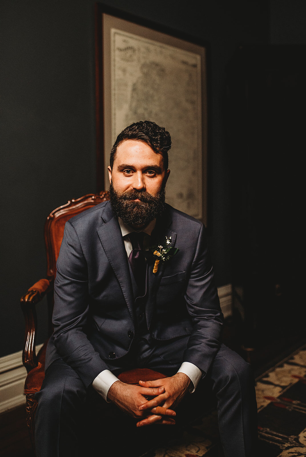 Groom sitting on a red leather chair and a gray suit for wedding portraits by Baltimore wedding photographers