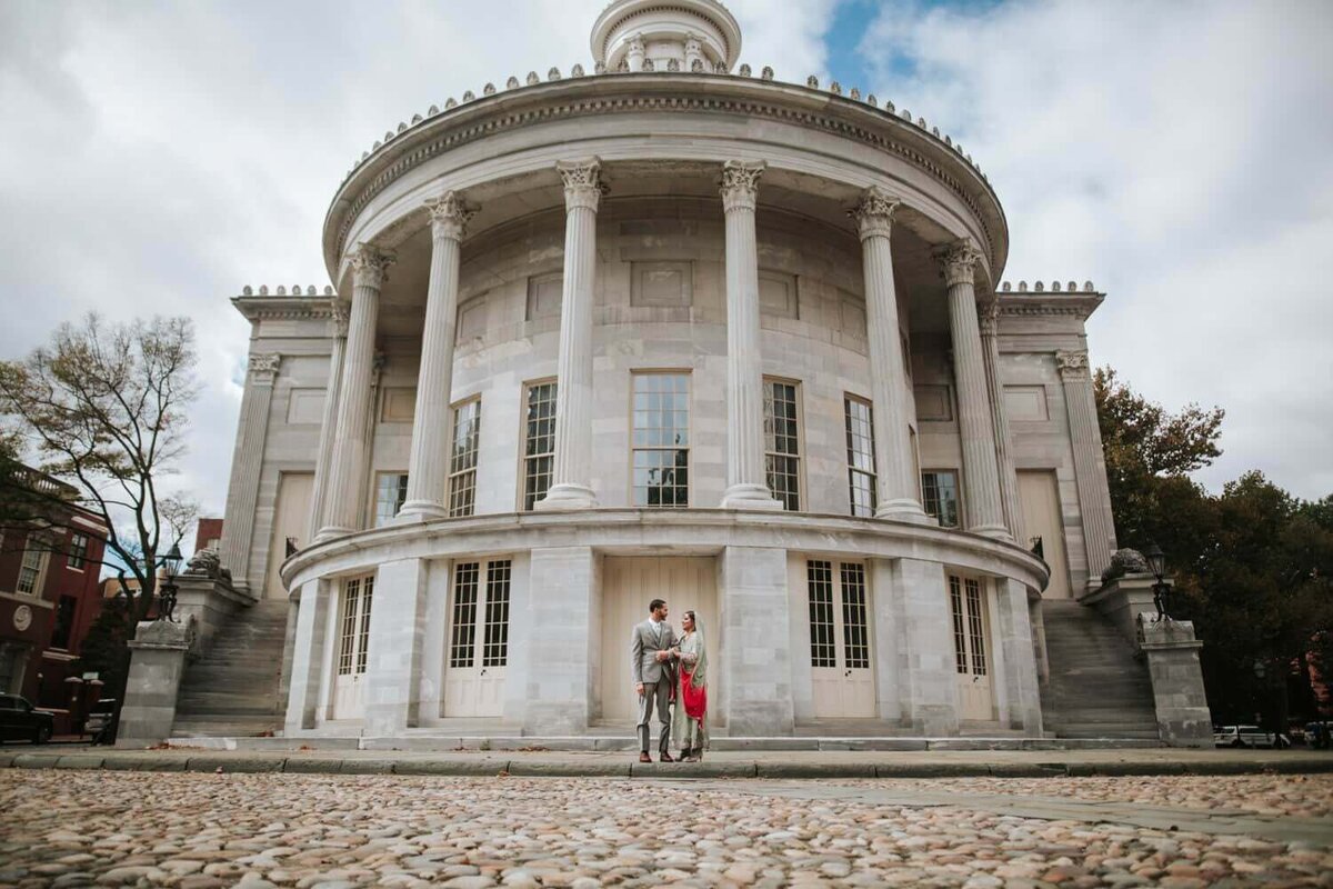 South Asian wedding bride and groom In old city Philadelphia taking portraits at the Merchant Exchange Building before their reception.