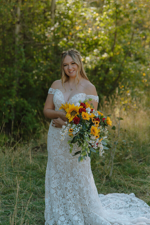 A bridal portrait of a woman on her elopement day. She's holding a bouquet of sunflowers and roses. The photo is cropped from the knees up.