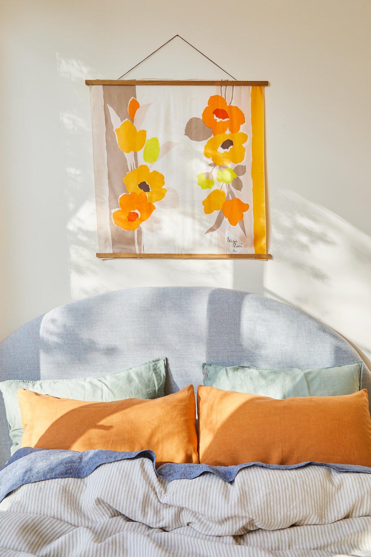 Detail of floral wall hanging and upholstered bedhead with orange cushions in Elwood apartment