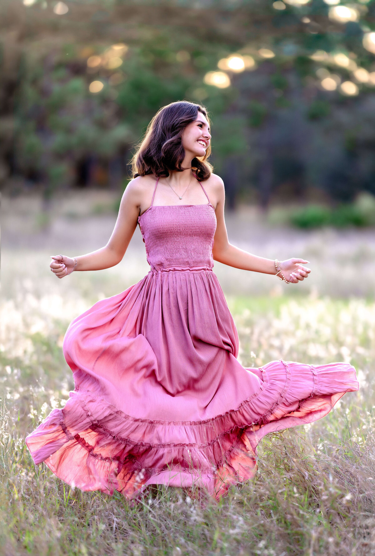 Senior girl in pink dress twirling with a natural smile during a Winder garden senior sunset session