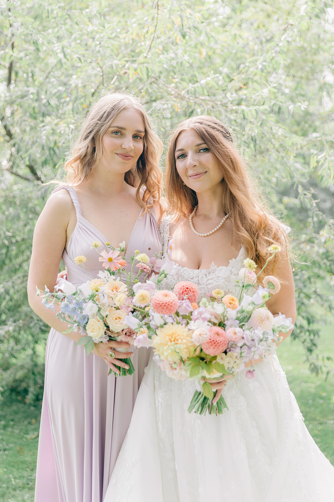 A bride and her bridesmaid smile in the garden of the Forest and Stream Club.