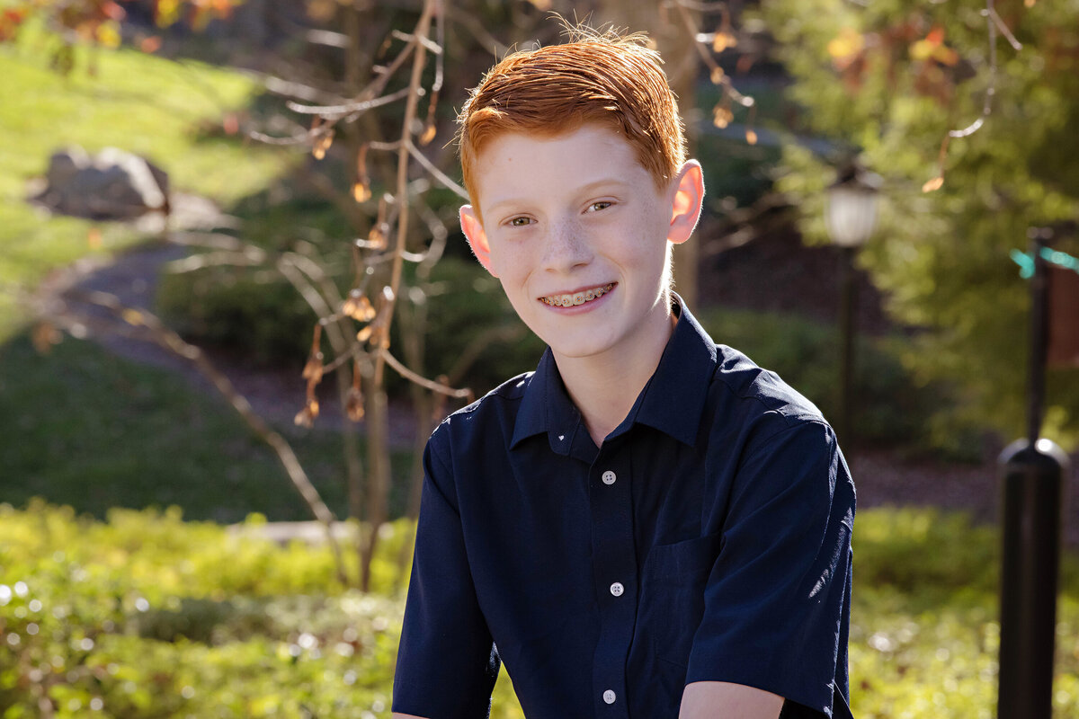 Handsome autumn portrait of red‑haired tween boy seated on bench in park at Ballantyne Corporate Park
