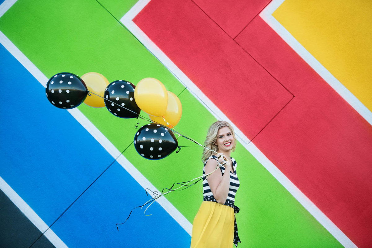 high school senior photo of girl in colorful outfit with balloons in front of rainbow background