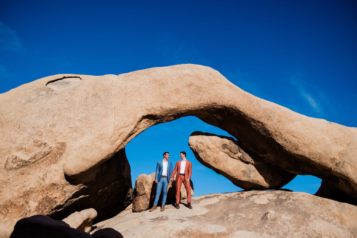 Two grooms stand on Arch Rock in Joshua Tree National Park.