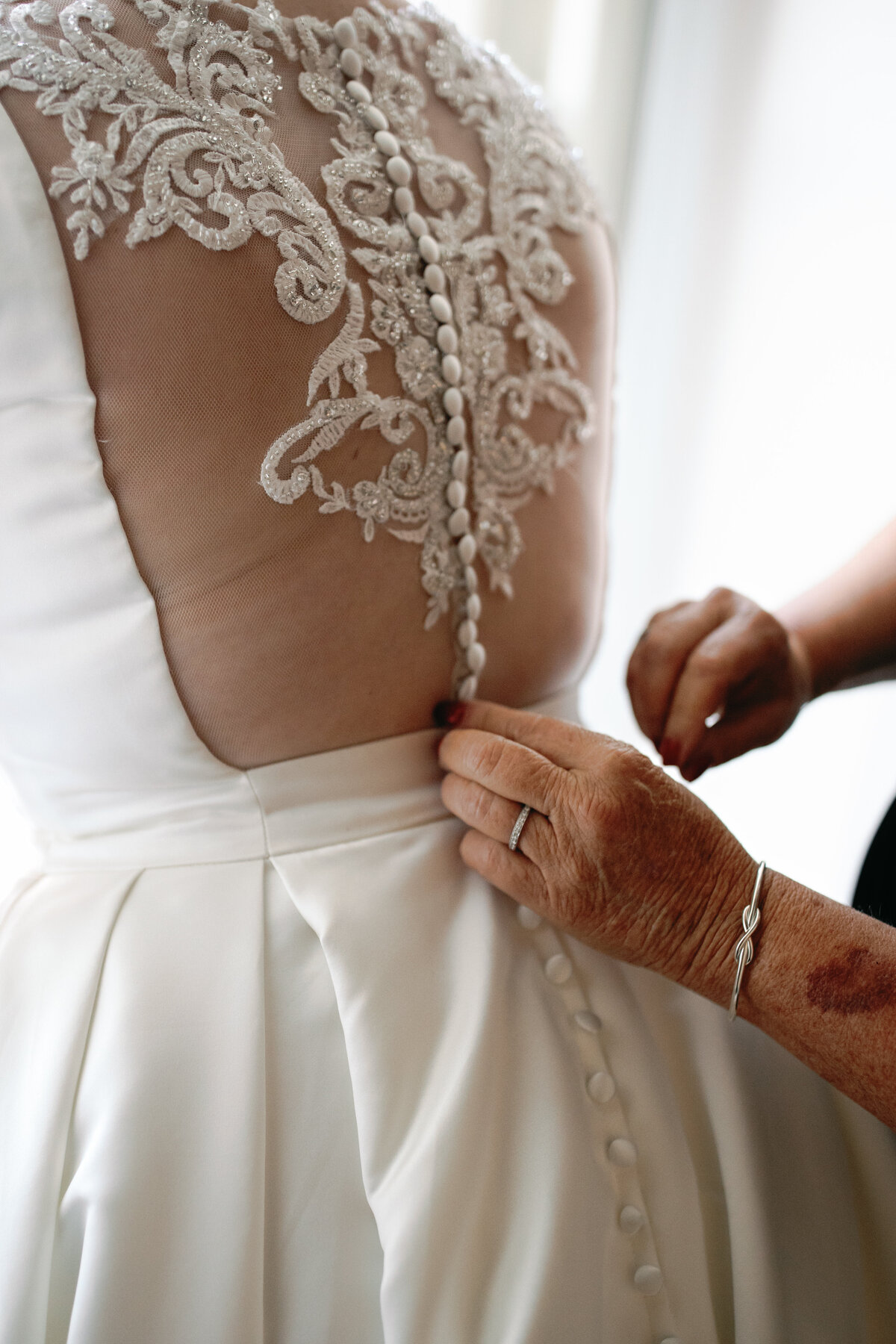 Close-up of satin ballgown with lace illusion back as bride gets buttoned into dress before DC wedding.