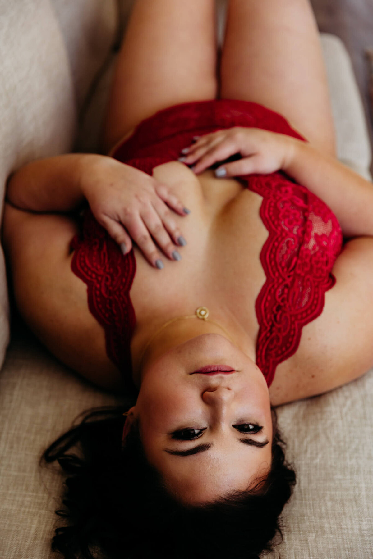 stunning woman in a red bodysuit laying on her back and looking up at camera with tons of confidence