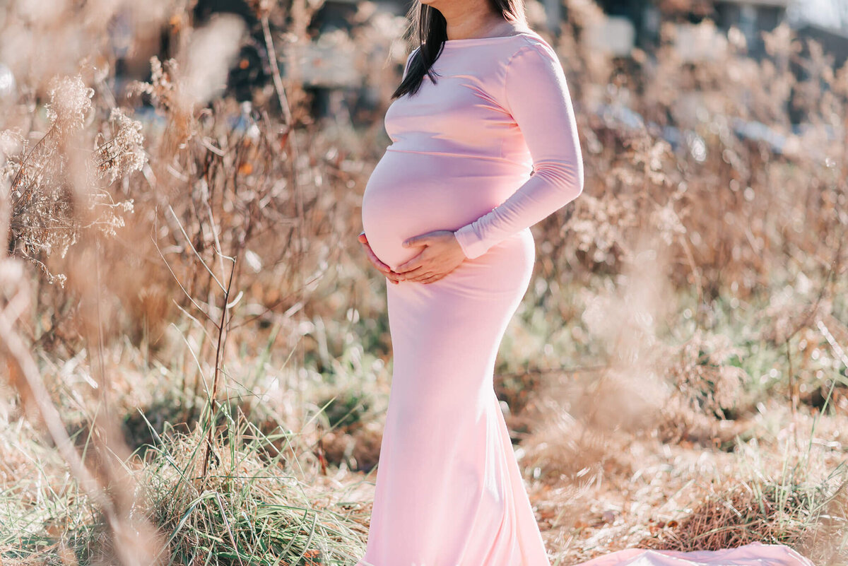 A close up belly of a woman wearing a light pink form-fitting maternity gown