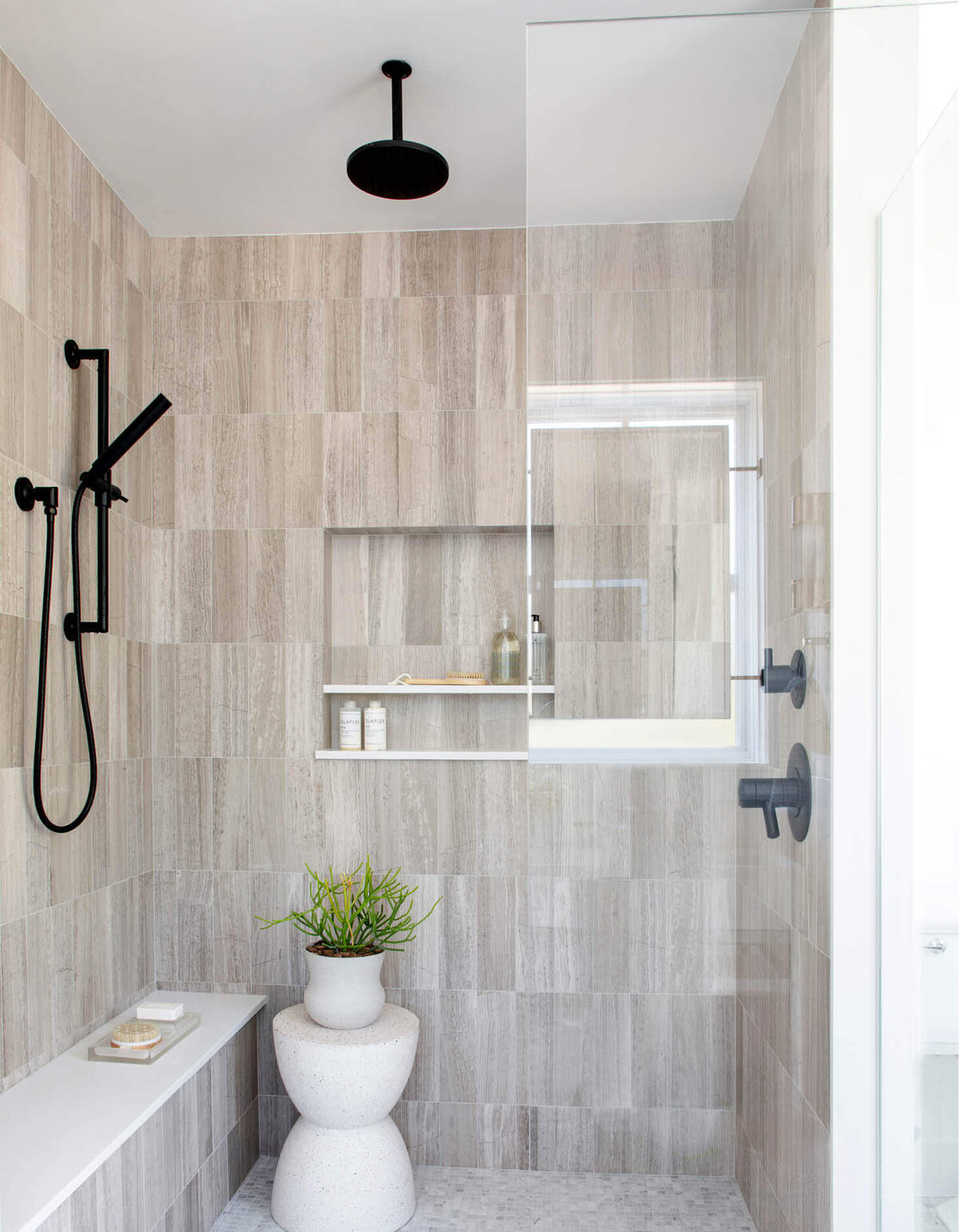 Milton interior design creates a primary bathroom with a walk-in shower, stone walls, mosaic tile flooring, and black Brizo fixtures in a new construction home.