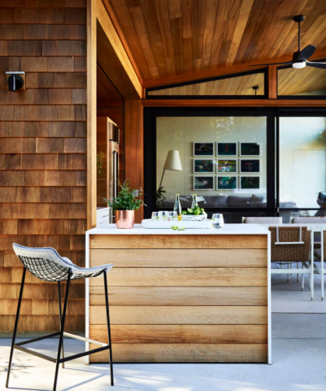 Interior decorators in Hingham create an outdoor kitchen with a waterfall island, red cedar siding, and modern furniture in a South Shore, Massachusetts home.