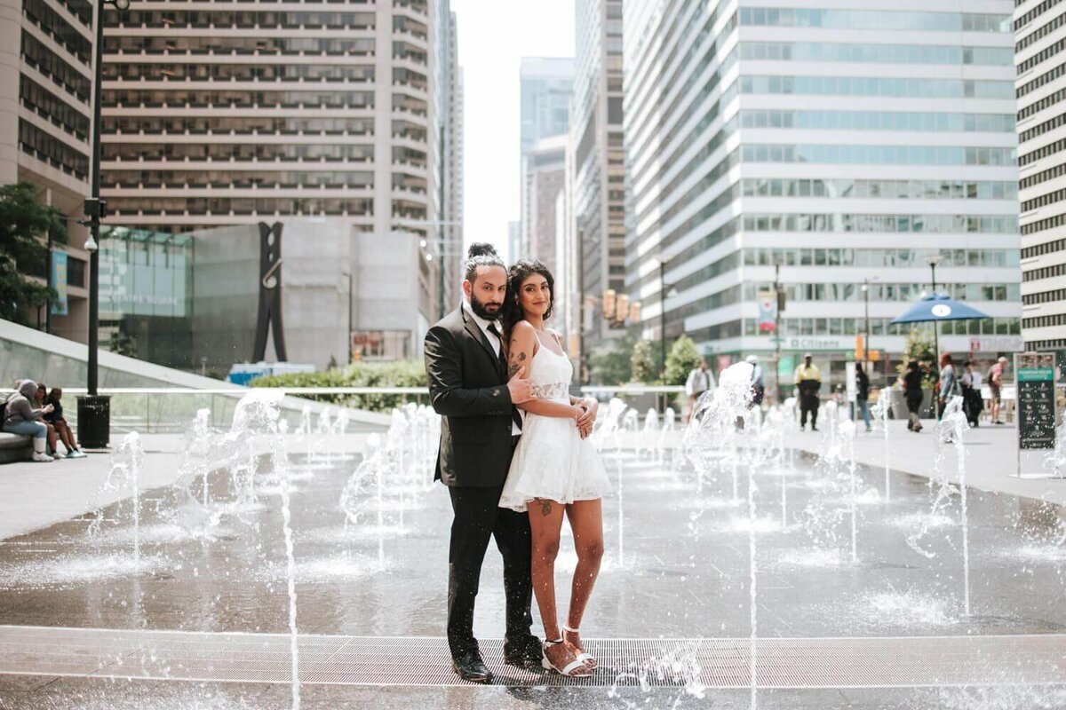 South Asian couple hugging each other in Philadelphia surrounded by fountains.