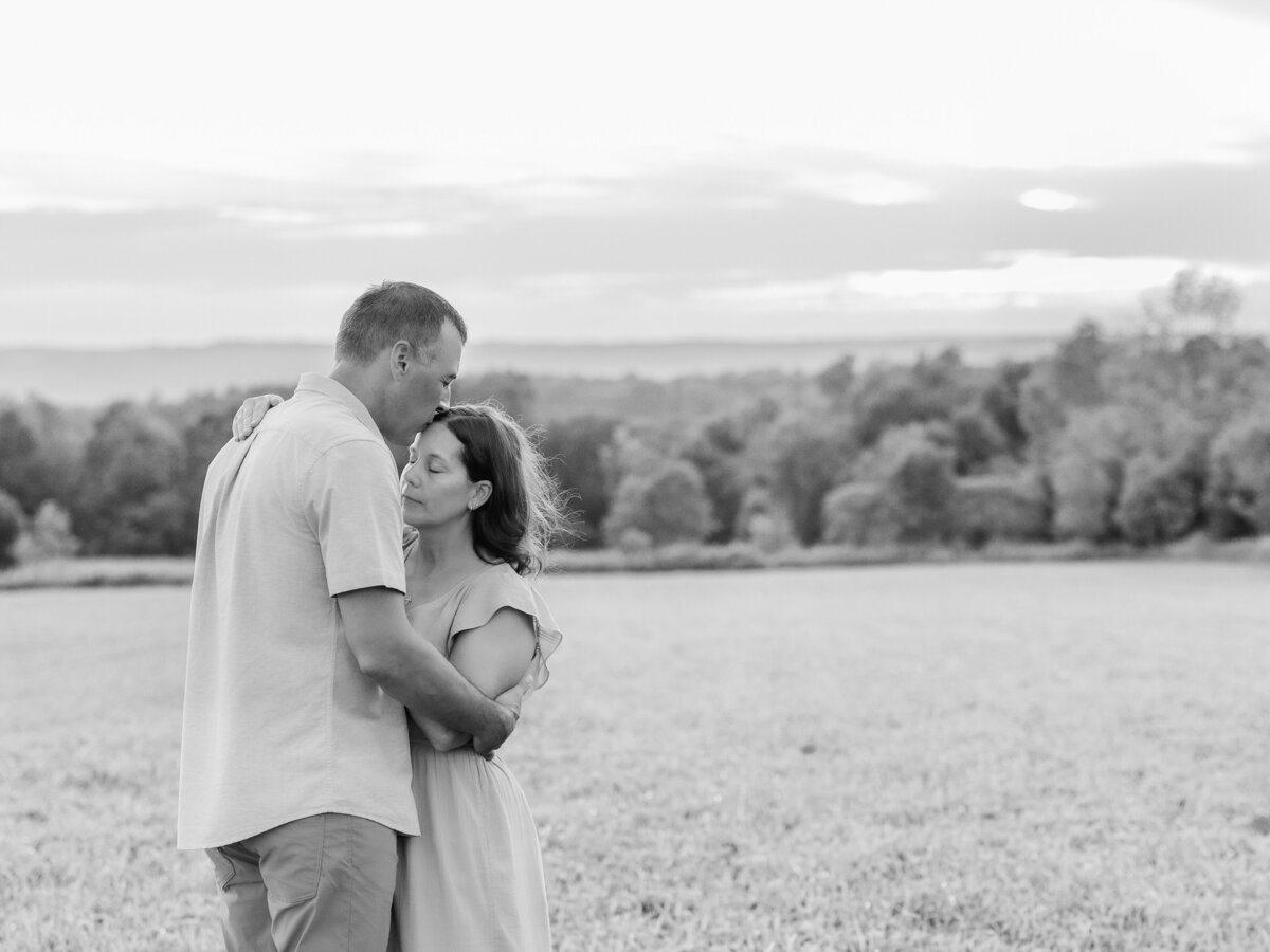 Husband kissing the top of his wife’s head in a field outdoors for couple’s photography.