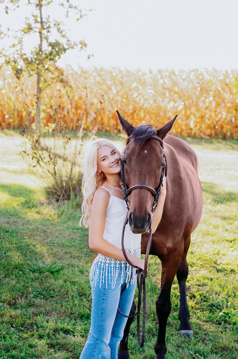 Country-style senior session with a girl and her horse, embracing in a natural field setting.