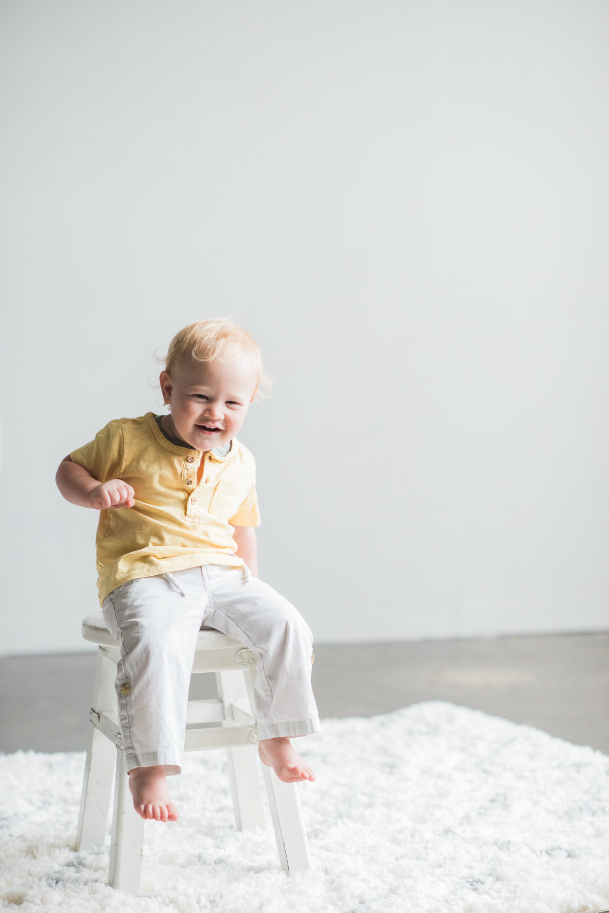 toddler boy laughing while sitting on white stool