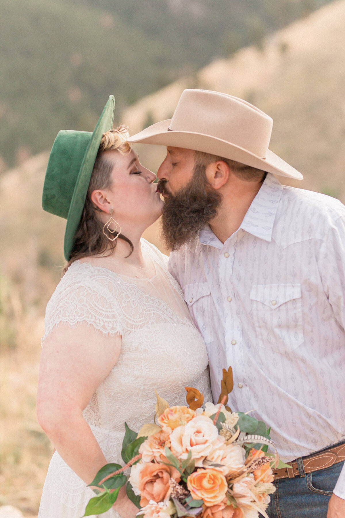 The bride, with her emerald green hat and coral bouquet, kisses her new husband .