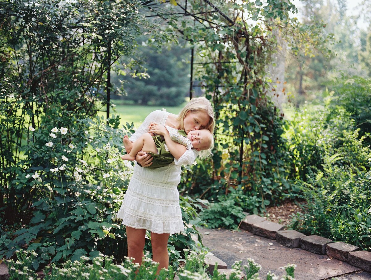 mom kisses baby girl during family photography session at park