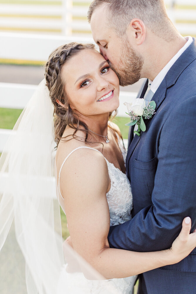 bride smiling as groom kisses her on the cheek