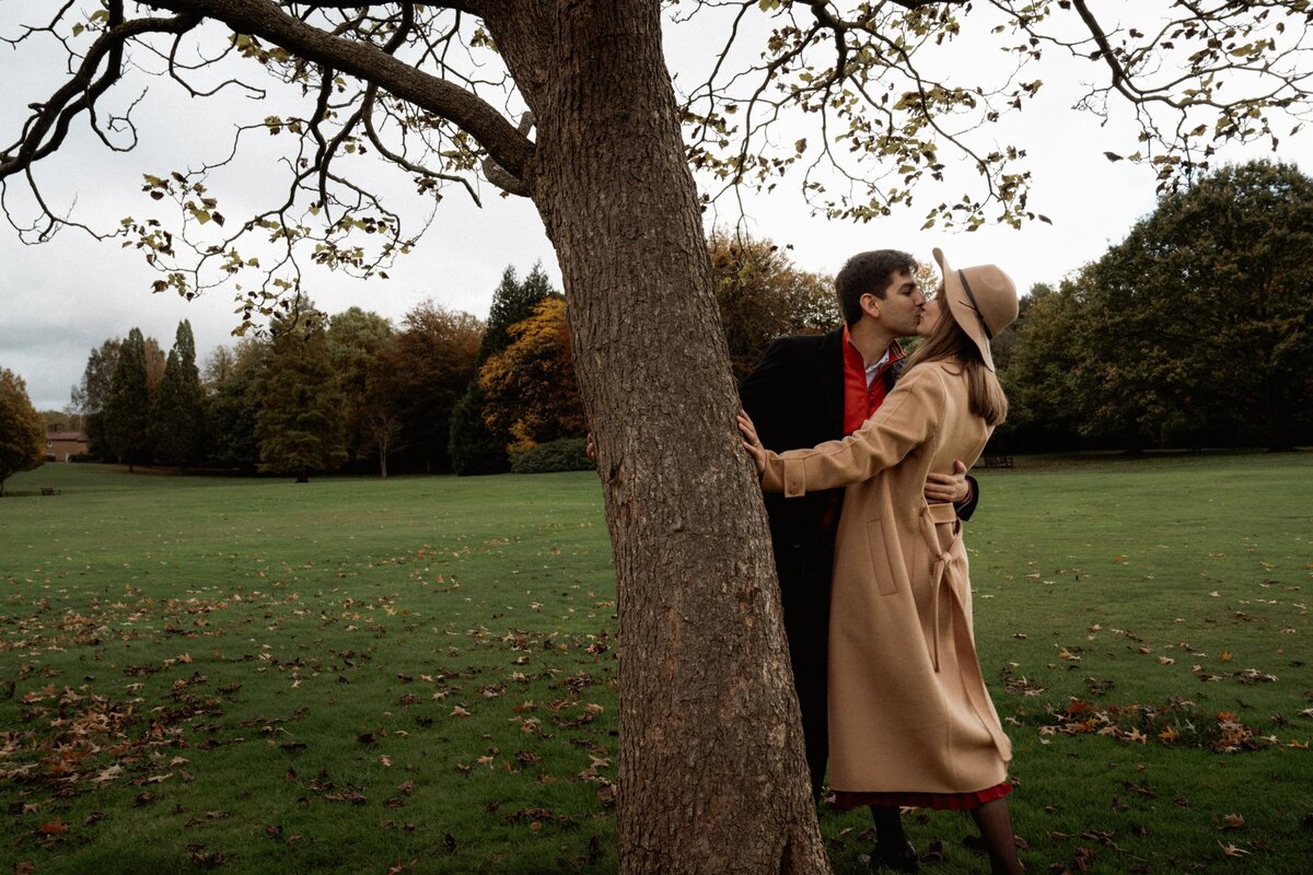 Couple standing next to a tree exchanging a romantic kiss during engagement photography in Hampstead Heath London