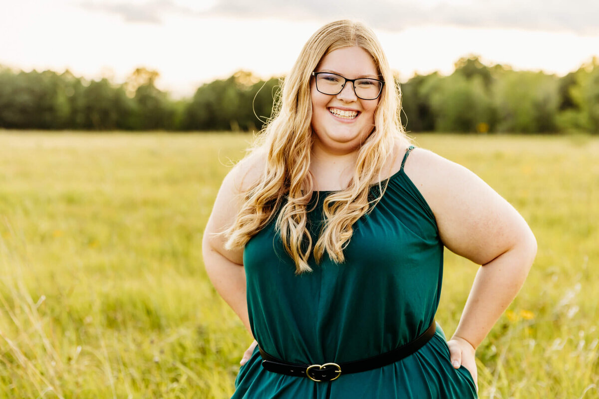 blonde high school girl with glasses in a teal jumpsuit laughing and enjoying her Oshkosh senior photography session