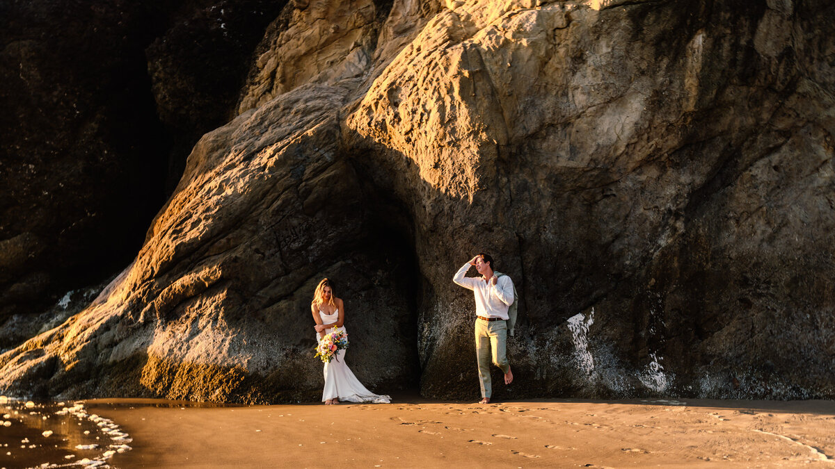 During their Oregon coast elopement, a bride and groom lean on a coastal rock , painted golden by the sunset.