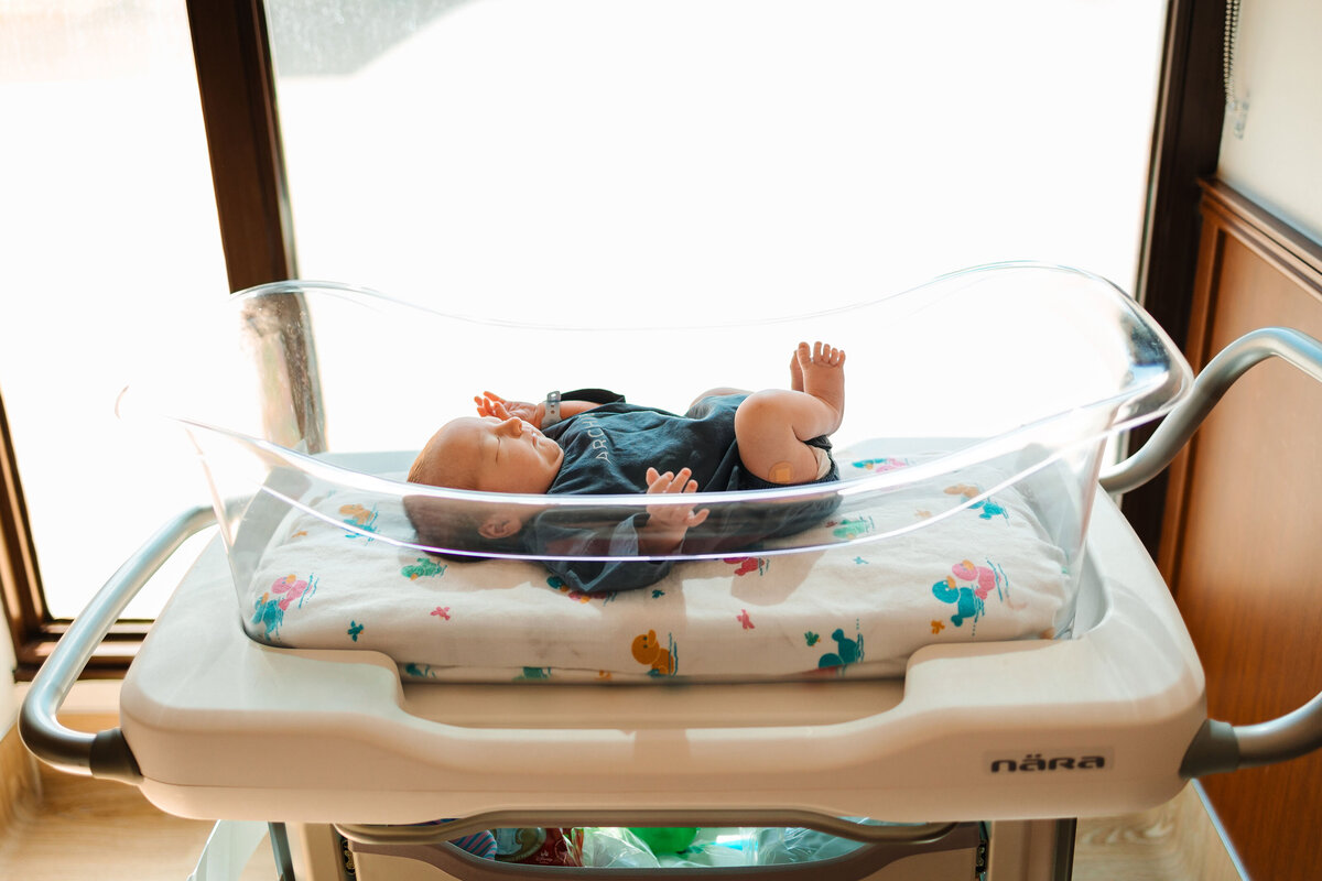 A serene photo of a newborn baby lying in a hospital cradle, dressed in a blue outfit and wrapped in a white blanket.