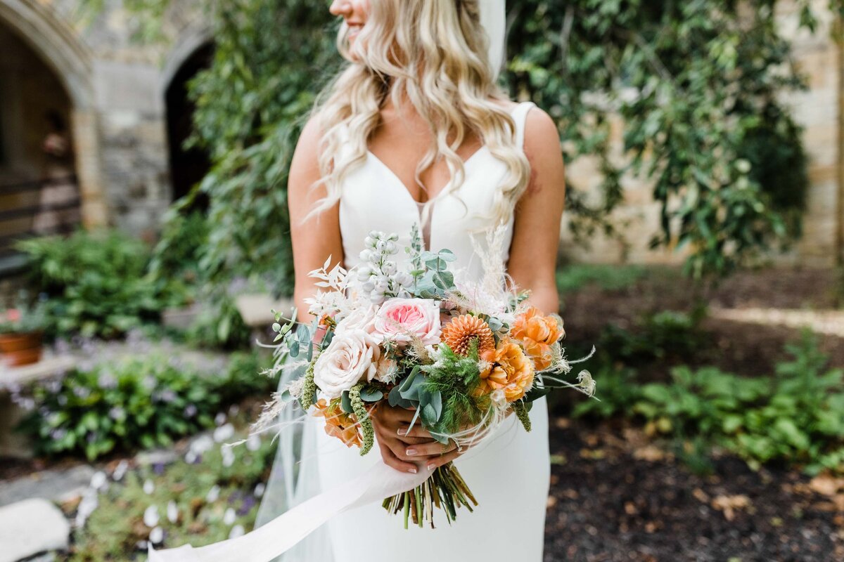 Bride holding a vibrant bouquet of orange and white flowers in an outdoor garden setting in South Bend.