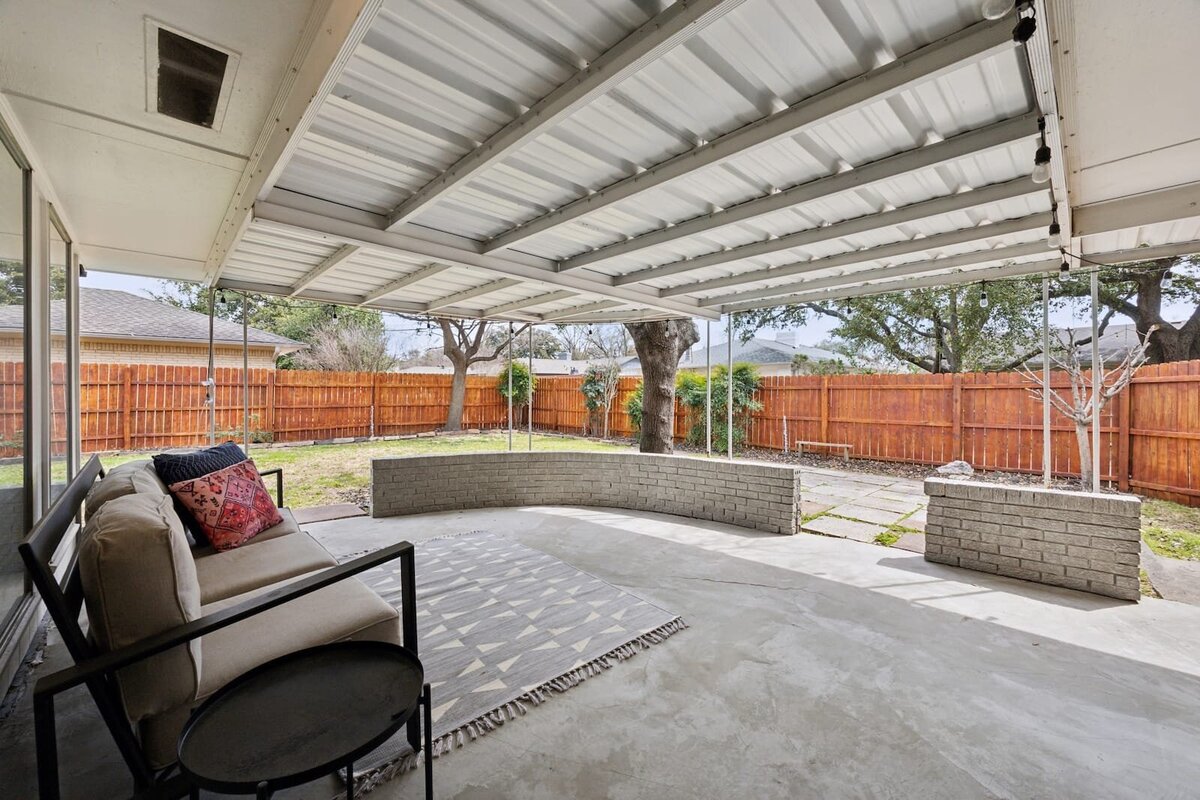 Covered concrete back patio at 3120 Chapel Downs Dr Dallas TX with string lights, seating area, and views of a private fenced yard — Haven Realty Group.