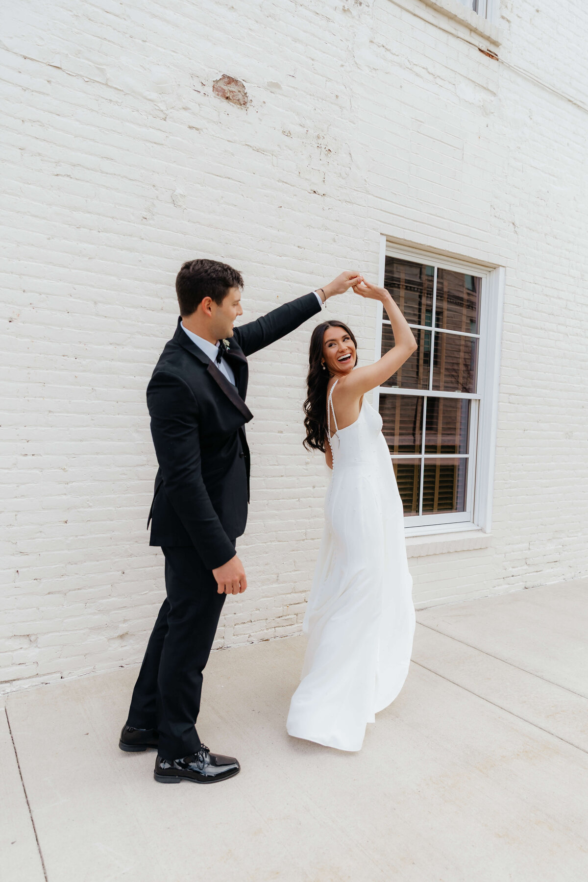 Bride twirling in white dress beside groom, bright and joyful wedding photography for couples who want relaxed elegance with personality