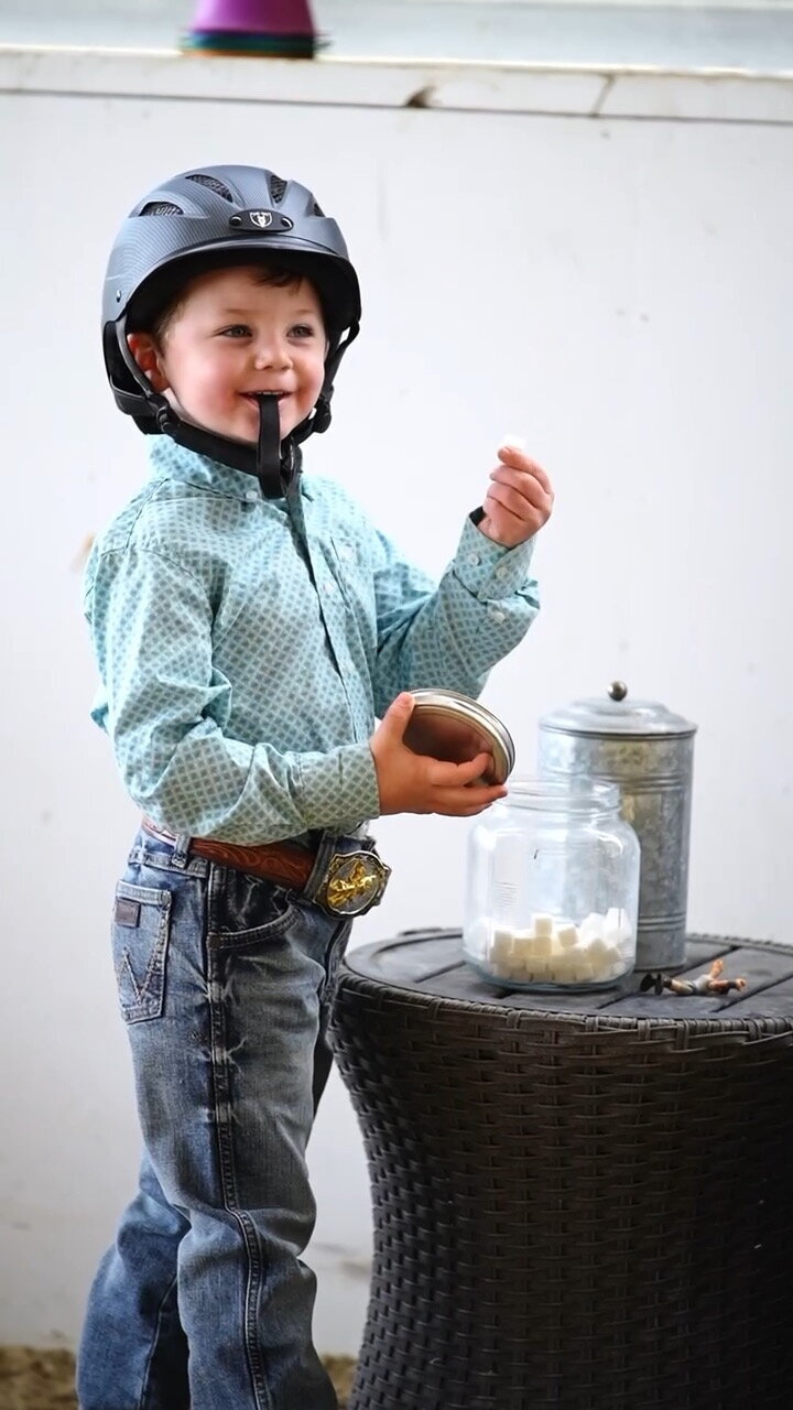 A young rider is removing a sugar cube from a jar to give to a horse