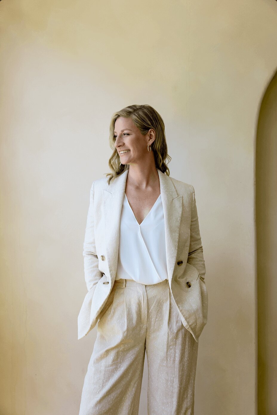 woman in a beige suite standing and looking out of a window