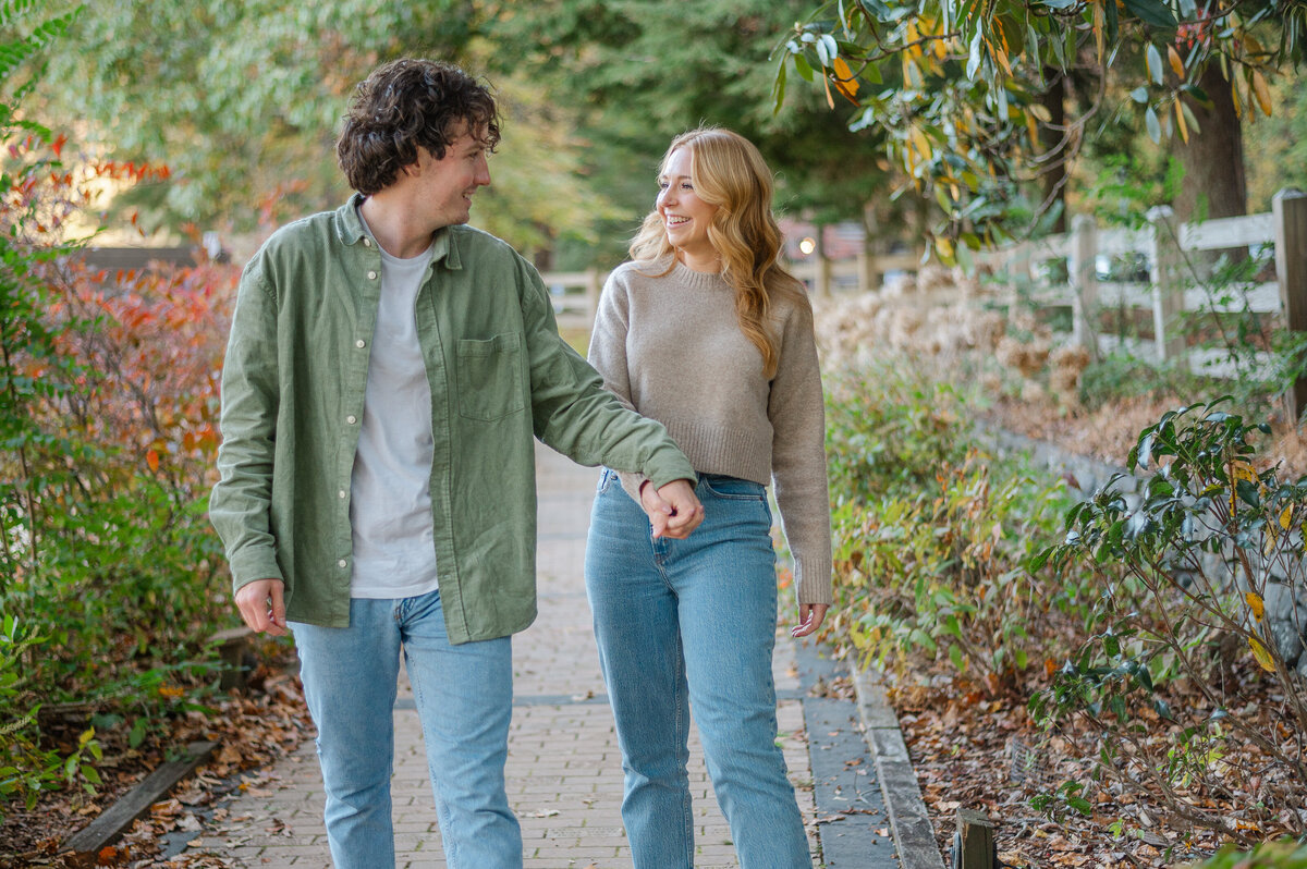 Couple look at each other and laugh as they walk hand in hand during their Fall engagement session in the North Georgia Mountains during their engagement photos