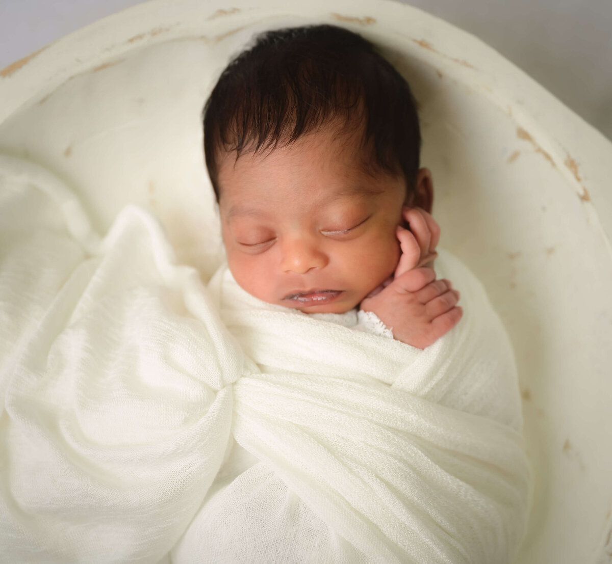 Baby wrapped in white cloth sleeping in a white bowl during his newborn photo session in his Kitsap Peninsula  home.