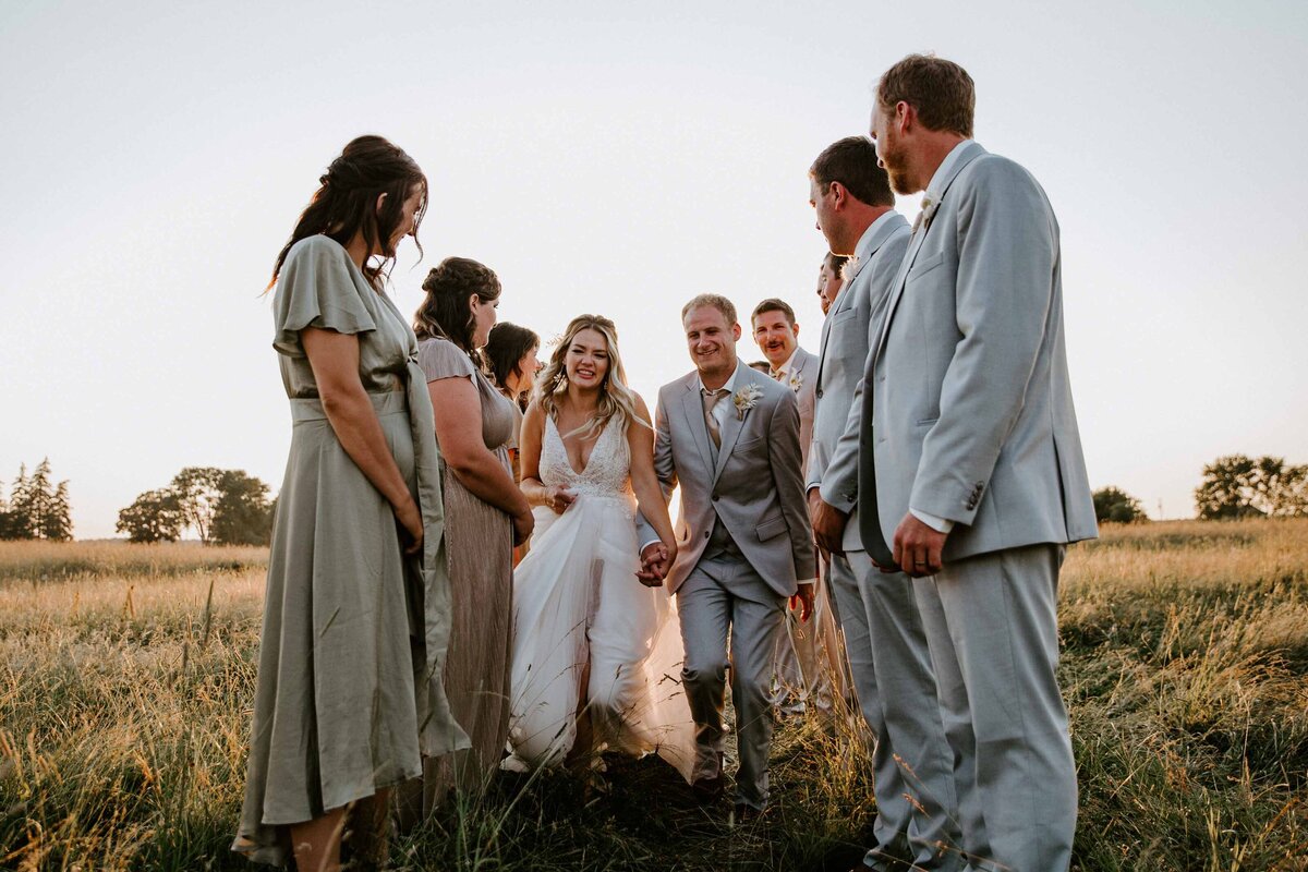 Bridesmaids and groomsmen form an aisle for rustic farm wedding in Exeter, Ontario. The Bride and groom are smiling and running between them.