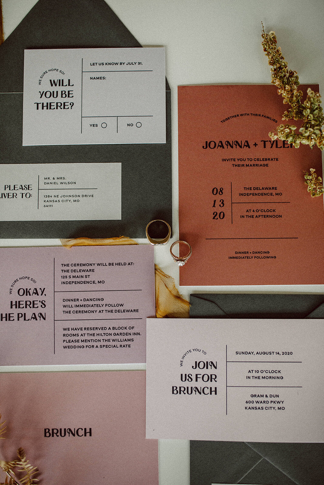 Peach, mauve, and off-white wedding stationery with black font atop and wedding bands with ribbon and stems.