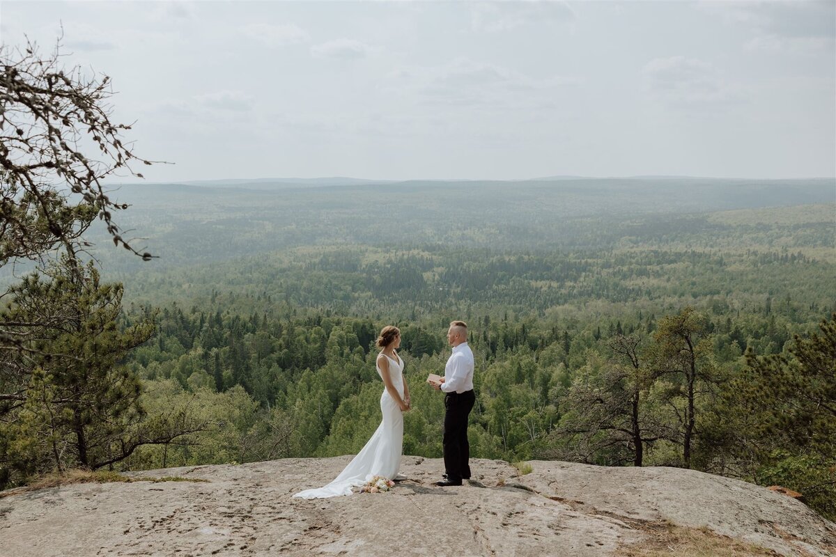 bride and groom eloping in Minnesota saying their vows in the lusten mountains on an overlook with pine trees in the background