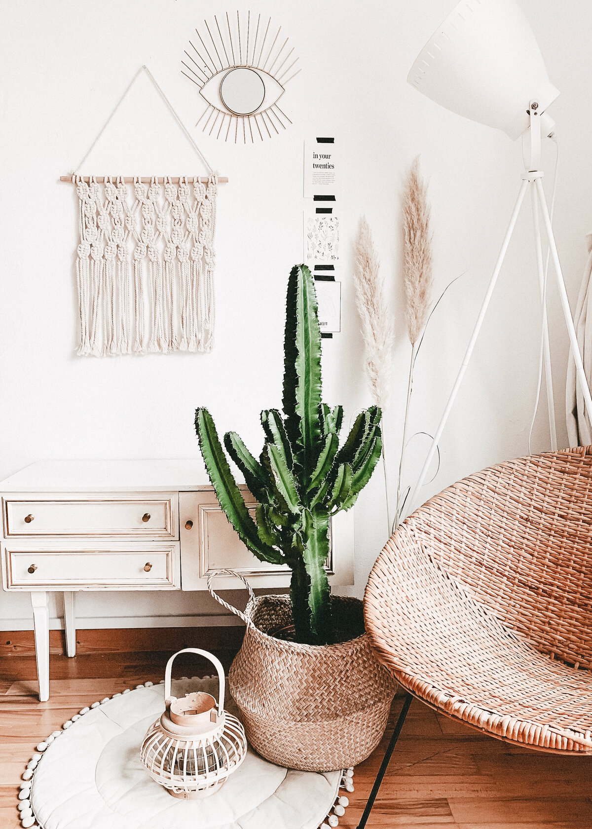 An interior photograph featuring a boho rattan chair, with macrame wall hanging and a cactus in a basket.