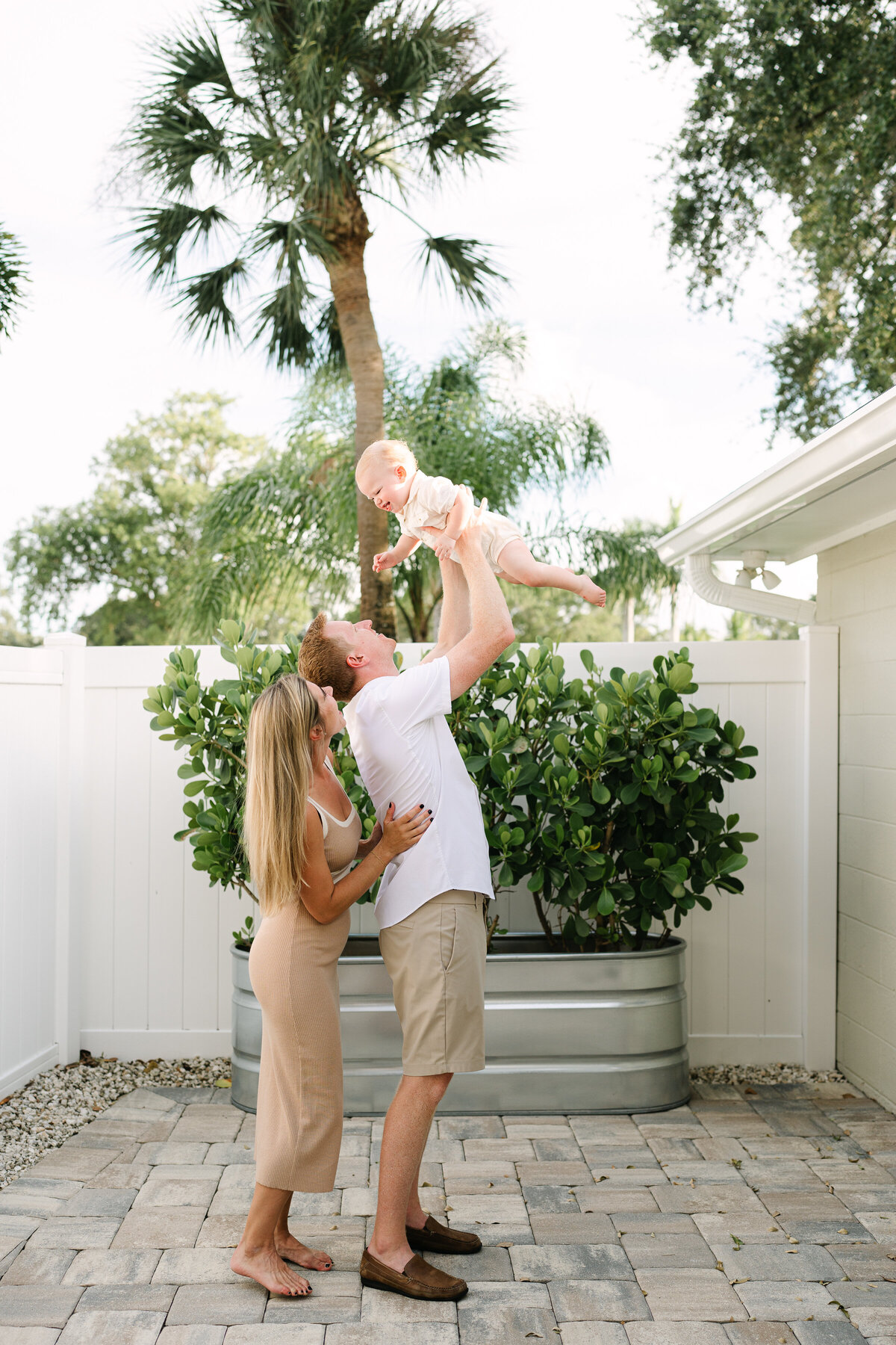 Couple tosses baby boy playfully in cozy back yard